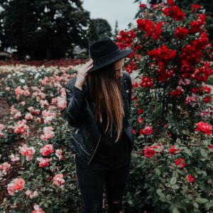 woman in black suit jacket and hat near field of pink and red roses